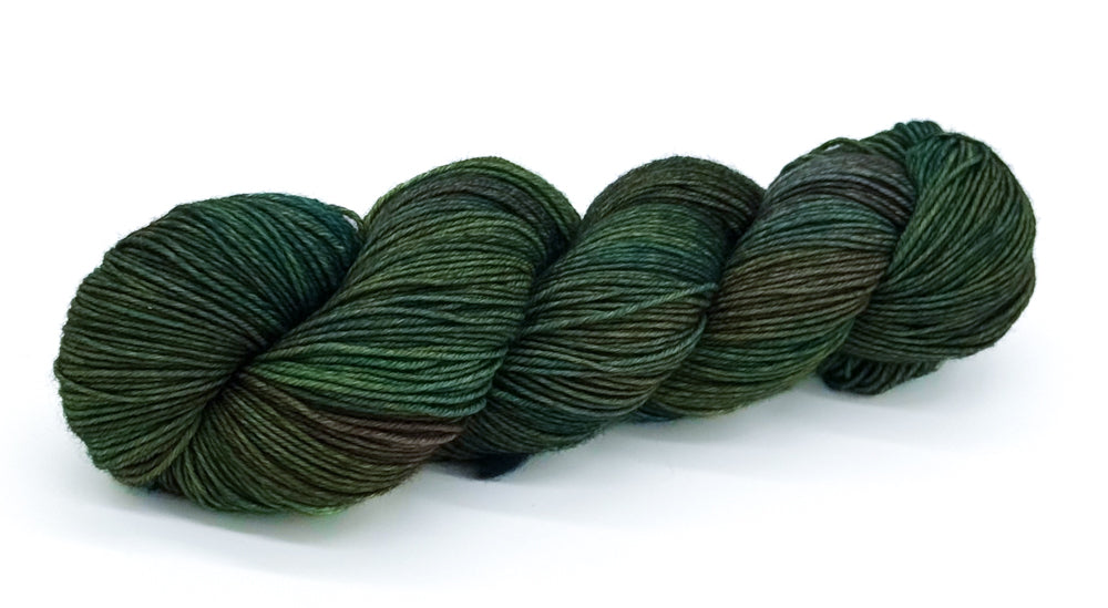 A skein of yarn in deep forest green shades with cool mossy tones.