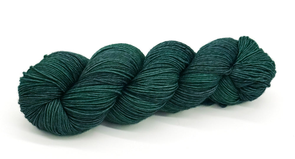 A skein of yarn colored in deep emerald and evergreen greens.