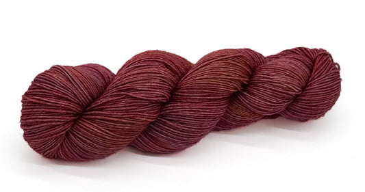 A skein of yarn shaded in soft mauve, dusty rose and aged parchment tones.